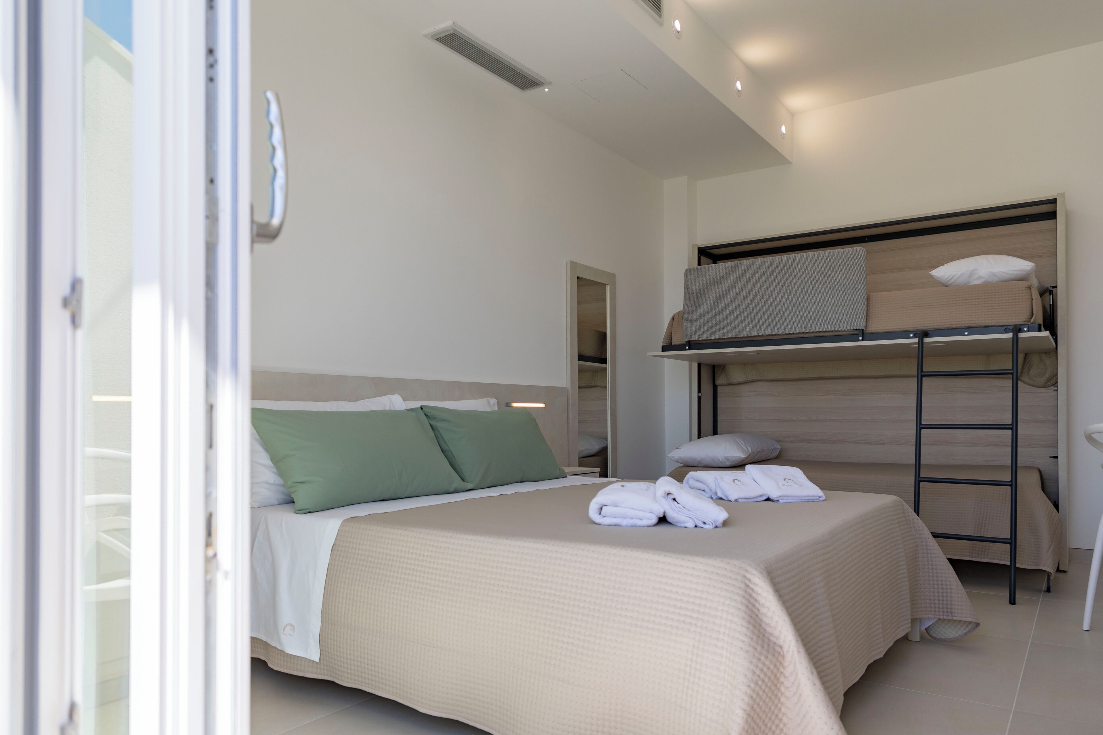 A hotel room with a bunk bed, a single bed, and a ladder. There are towels on the beds.