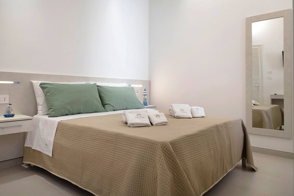 A neatly made bed with a beige bedspread, two pillows, and a set of towels.