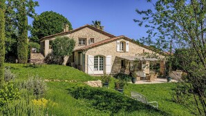 Une maison en pierre avec un toit en pente, un porche à l’avant et un jardin agrémenté d’un banc.