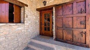 Ein Steinhaus mit Holztür und -fenster, einer Holztreppe und einem Laternen darüber.