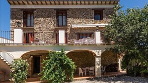Ein zweistöckiges Steinhaus mit Balkonen, Sitzgelegenheiten im Freien und einer überdachten Terrasse.