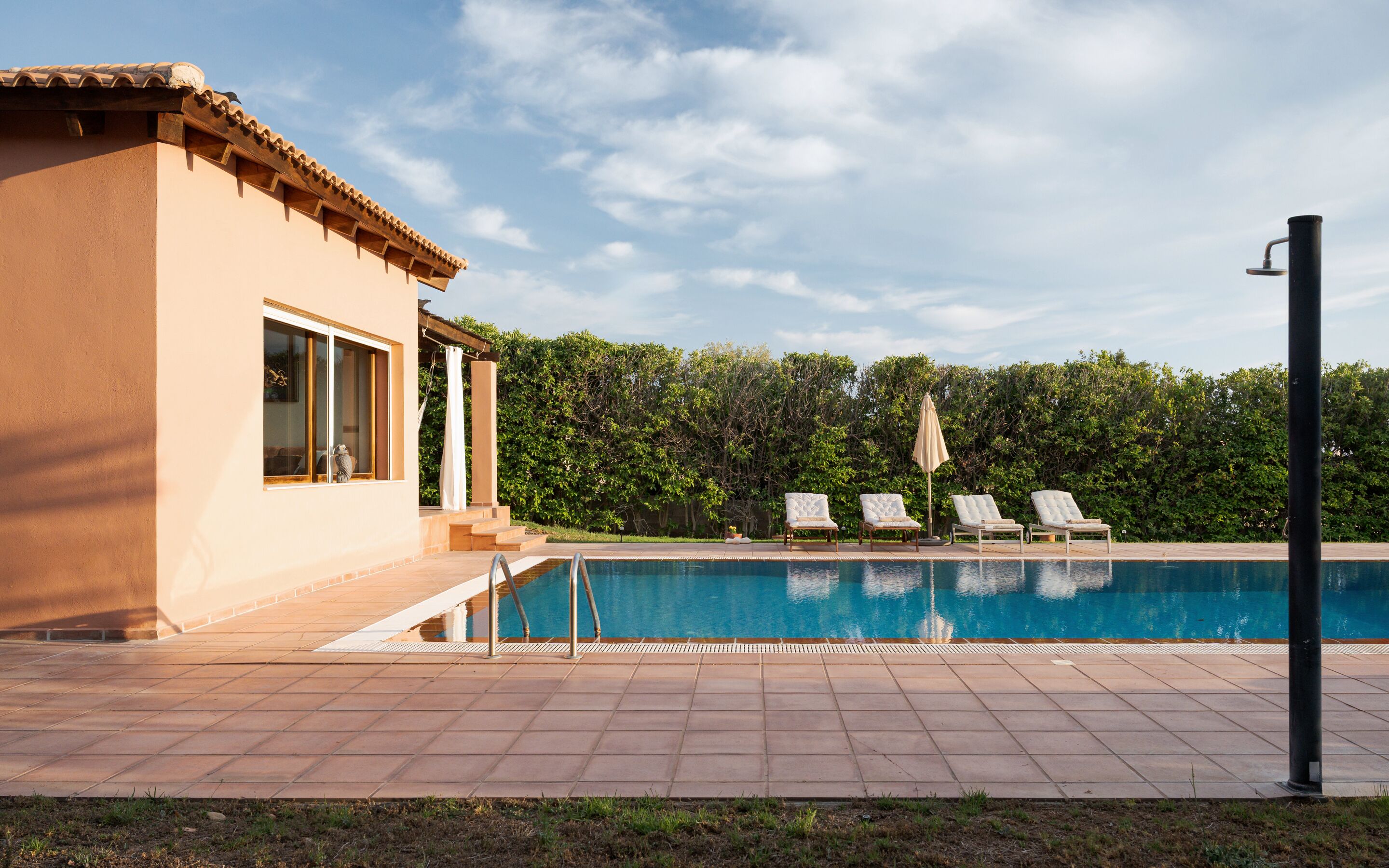 Una piscina con cuatro sillas de descanso, una pérgola y un patio cubierto.