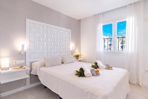 A hotel room with a large bed, a bedside table with a lamp, a window with curtains, and a view of buildings outside. - Luxury Family Riviera Del Mar (Mijas)
