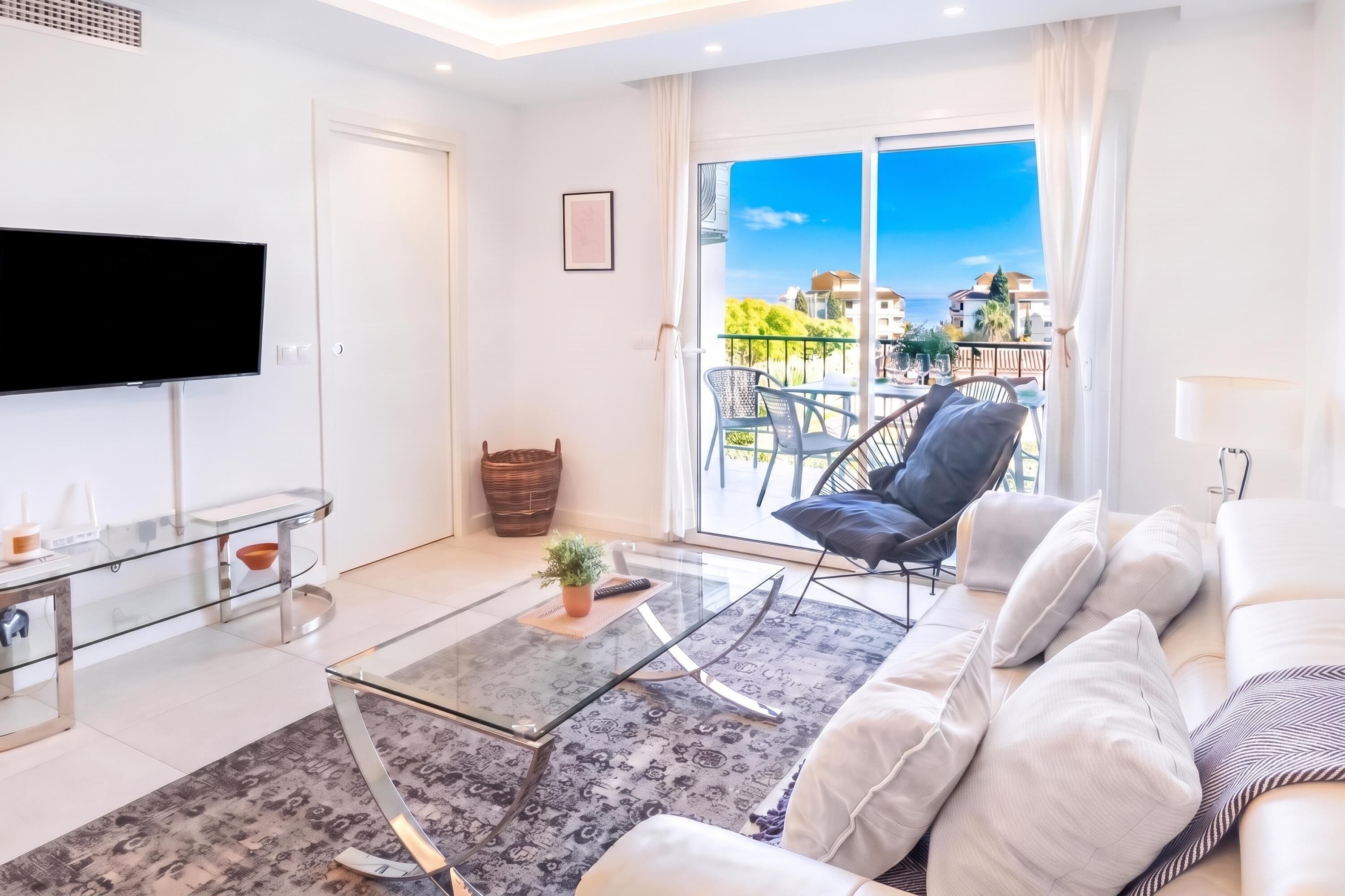 A modern living room with a glass coffee table, a sofa, and a TV mounted on the wall.