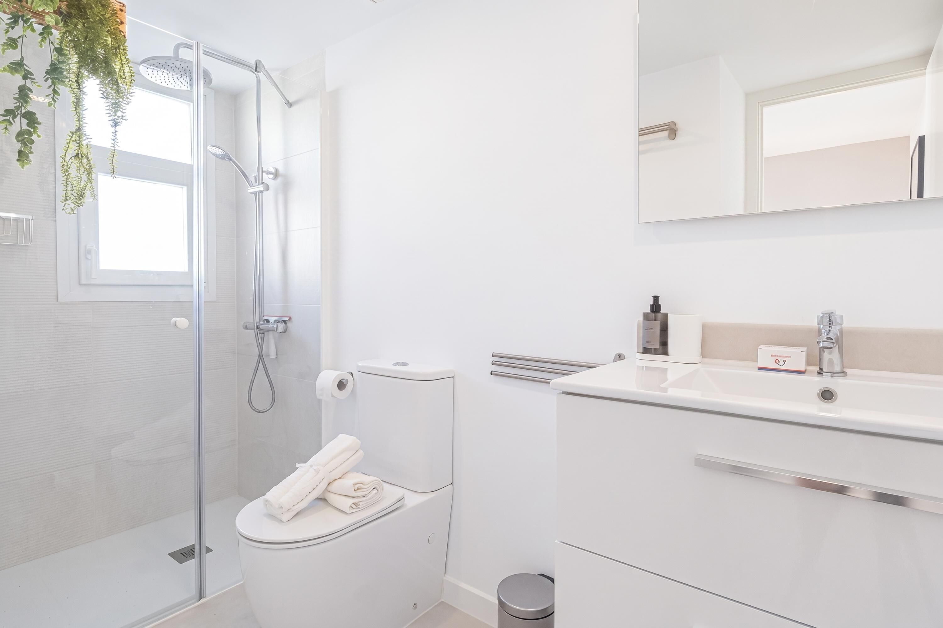 Een moderne badkamer met een glazen douchecabine, een toilet met een handdoek en een wastafel met een spiegel.