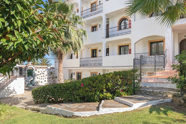 A multi-story building with balconies, a stone wall, and a well-maintained garden.