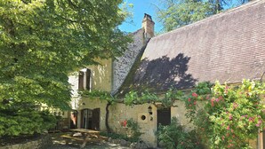 A rustic stone building with a sloped roof, a wooden bench, and a gravel courtyard.