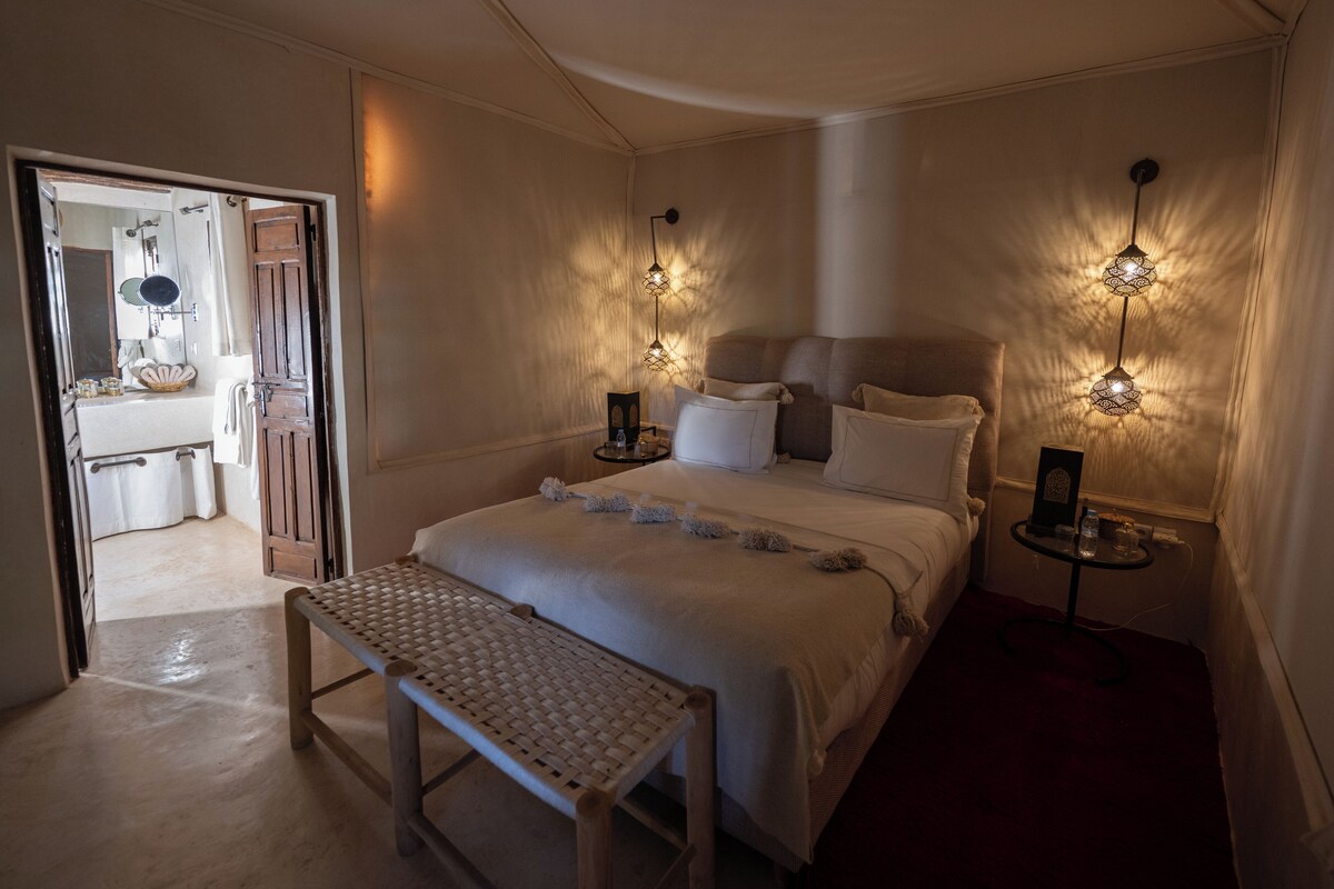 A bedroom with a large bed, bedside tables, a bench, and wall-mounted lamps.