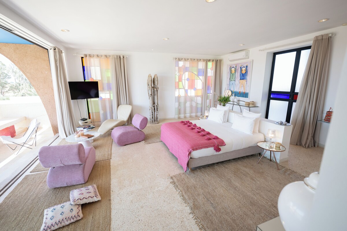 A modern hotel room with a large bed, a desk, a chair, and a TV.