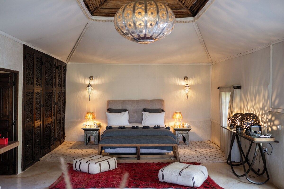 A bedroom with a large bed, two bedside lamps, a decorative ceiling light, and a red rug.