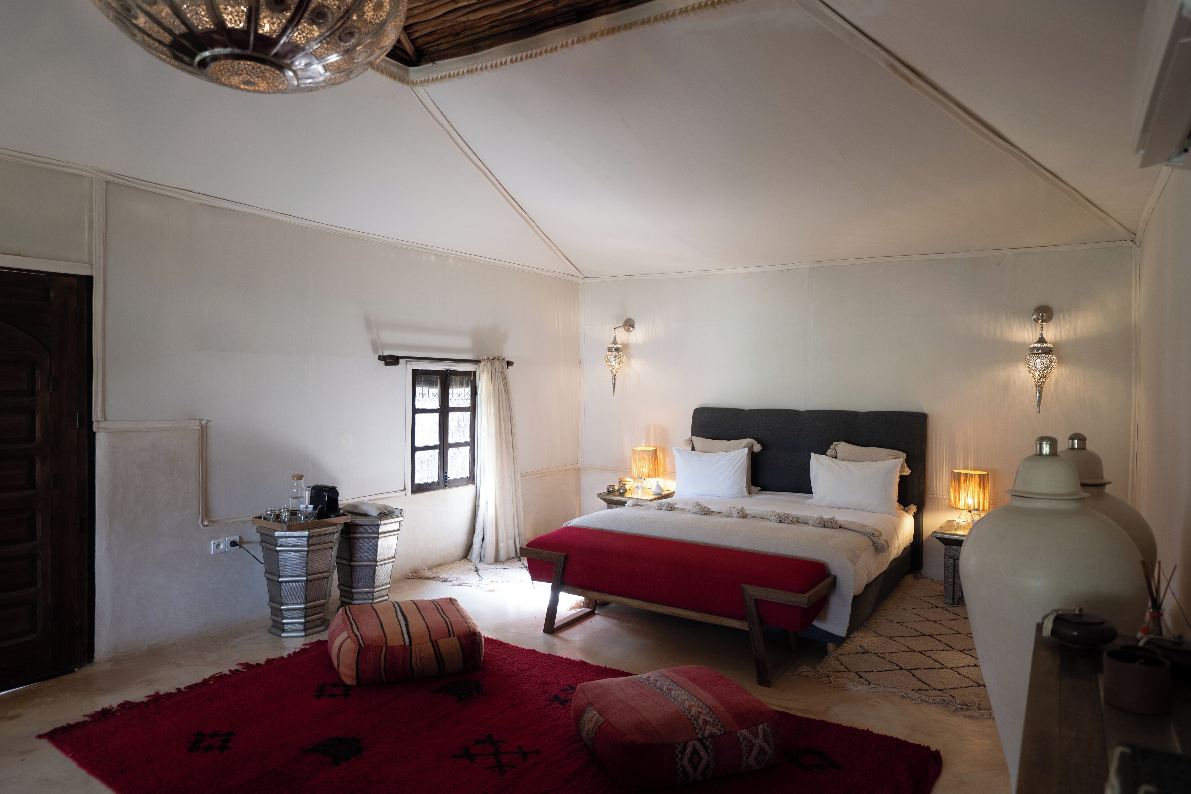A bedroom with a large bed, bedside lamps, a red rug, and a wooden door.