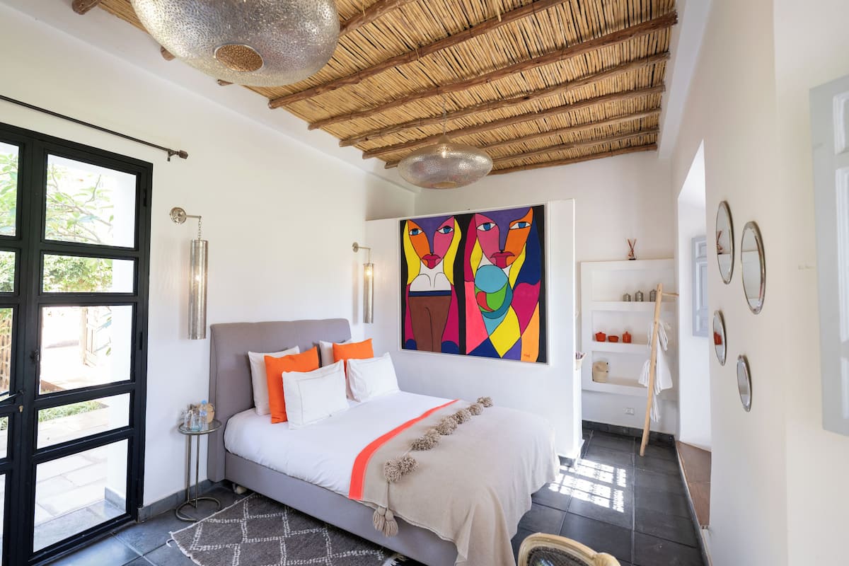 A modern bedroom with a bed, a large window, a ceiling fan, and artwork on the wall.