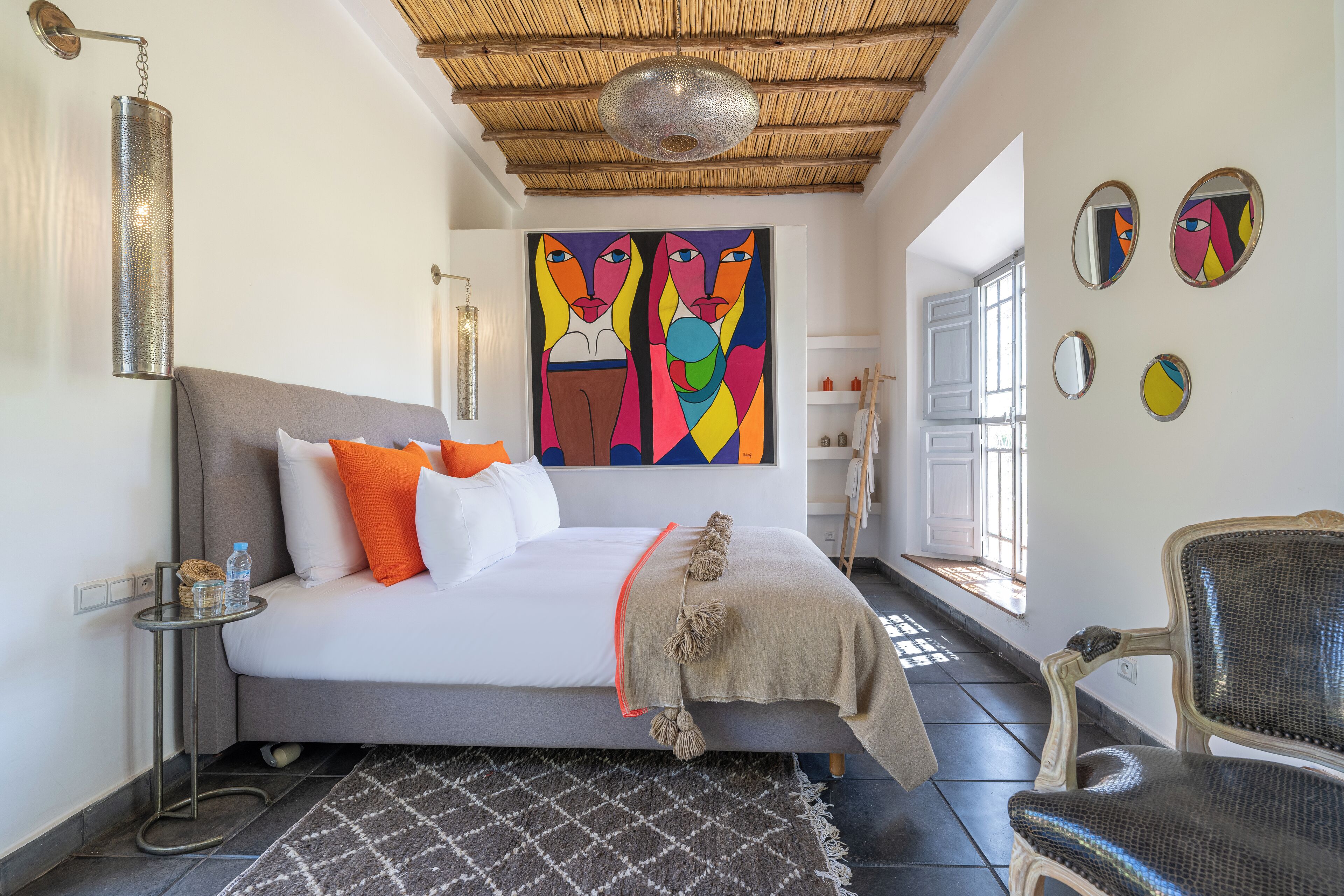 A modern bedroom with a bed, pillows, a side table, a chair, a rug, and artwork on the walls.