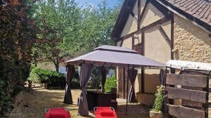 A covered outdoor seating area with two red lounge chairs, a table, and a wooden bench. - Charming Cottage with Pool and Private Parking in Périgord Noir (Berbiguières)