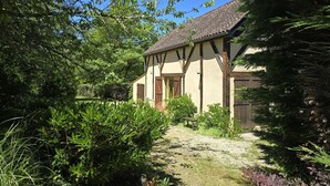 A traditional building with a tiled roof, surrounded by lush greenery and a gravel path. - Charming Cottage with Pool and Private Parking in Périgord Noir (Berbiguières)