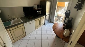 A compact kitchen with a sink, microwave, and oven. A dining area with a table and chairs is visible through an open door. - T3 Apartment 6 ppl, terrace and parking 30m from beach (Collioure)