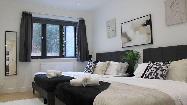 Ein modernes Schlafzimmer mit zwei Betten, einem großen Fenster mit Vorhängen, einer Heizung und Kunstwerken an den Wänden.