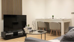 Ein modernes Wohnzimmer mit Flachbildfernseher, Couchtisch, Sofa und einem Essbereich mit Stühlen und einem kleinen Tisch.