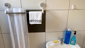 Un baño con un lavamanos blanco, dos botellas de jabón líquido, una pastilla de jabón y un perchero con dos toallas.