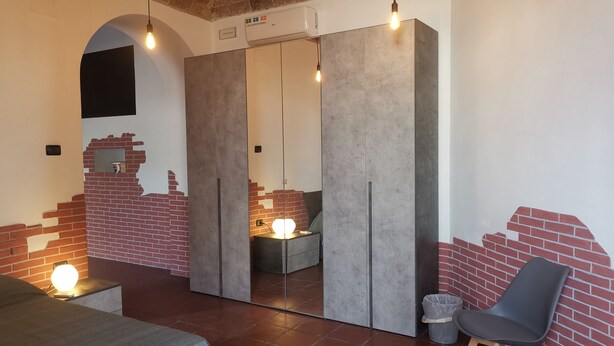 Ein modernes Zimmer mit Ziegelwand-Design, einem großen Spiegel, einem Bett, einem Sessel und einem kleinen Tisch mit Lampe.