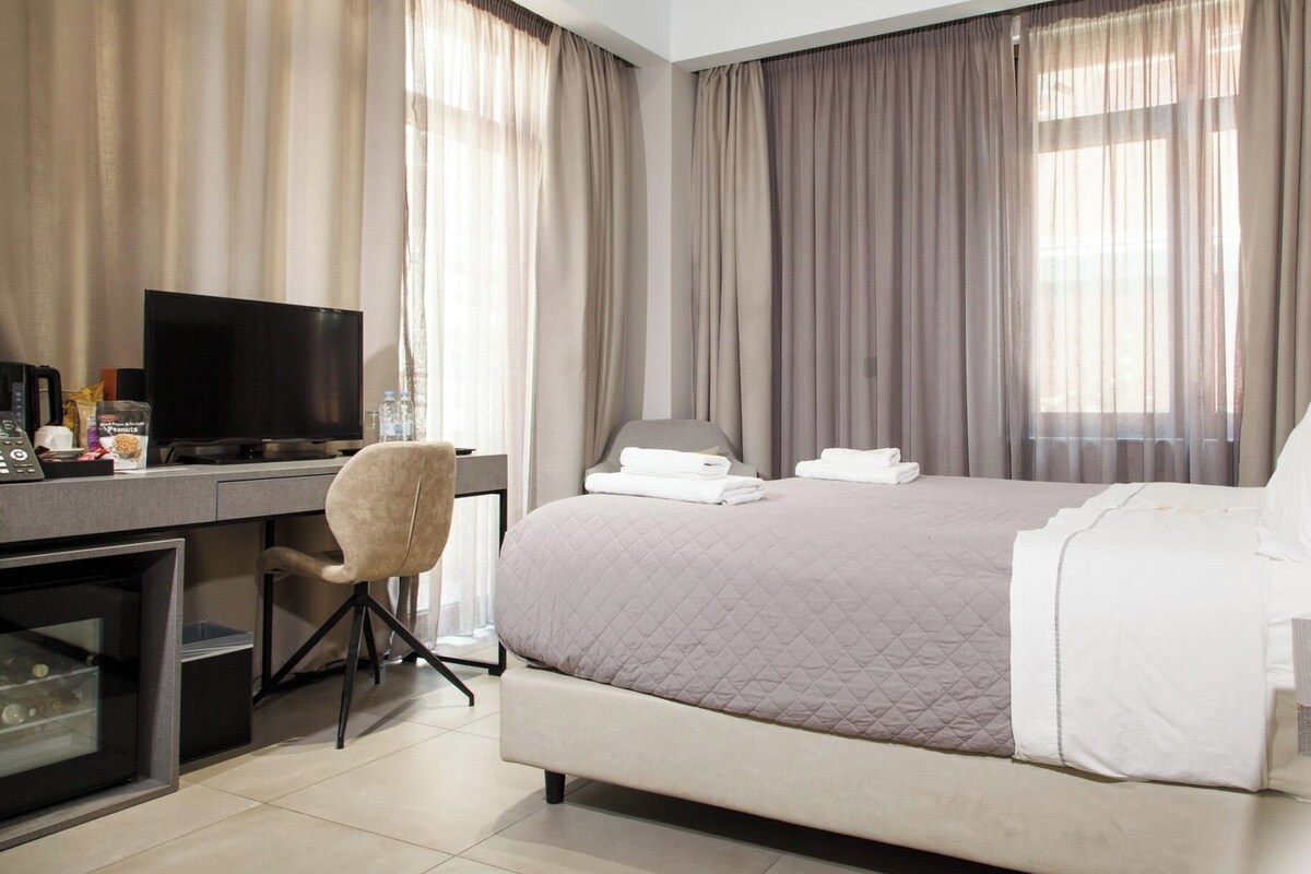 A hotel room with a bed, a desk with a TV, a chair, and curtains.