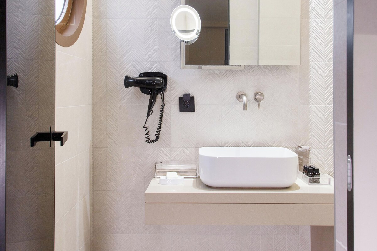 A modern bathroom with a vanity, a mirror, a hairdryer, and a towel rack.