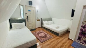 A small, triangular room with two single beds, a door with a 'No Smoking' sign, a clock, and a window with a plant. - Capital O 91167 Gemilang Candi Resort (Merbok)