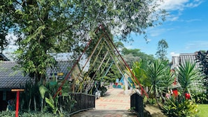 A pathway leading to a building with a traditional tiled roof, surrounded by lush greenery and a metal fence. - Capital O 91167 Gemilang Candi Resort (Merbok)
