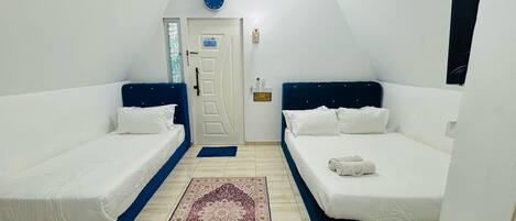 A room with two single beds, a door with a smoke alarm, a clock, and a small rug.