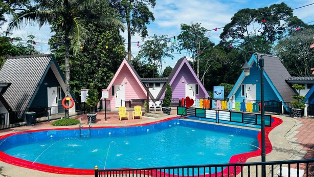 A swimming pool surrounded by colorful houses with a fence and chairs. - Capital O 91167 Gemilang Candi Resort (Merbok)