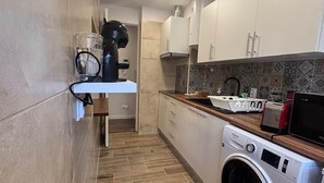 A compact kitchen with a built-in washing machine, a countertop with a toaster and a kettle, and a small shelf with a coffee maker.