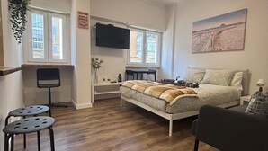 A bedroom with a bed, a desk, a chair, a TV, and a painting on the wall.