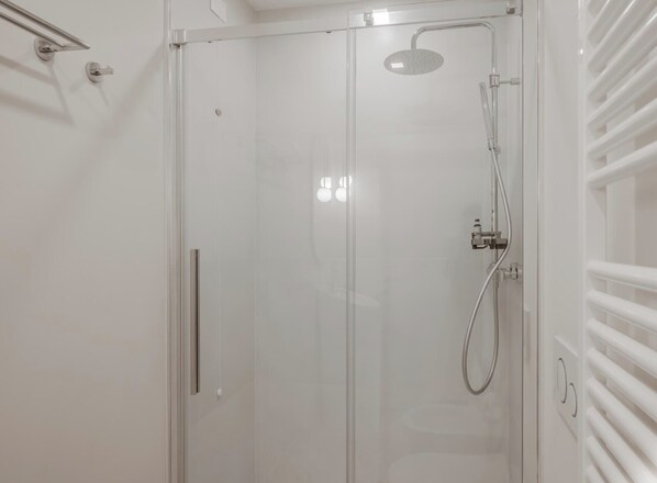 A modern shower enclosure with a glass door, a handheld showerhead, and a wall-mounted towel rack.