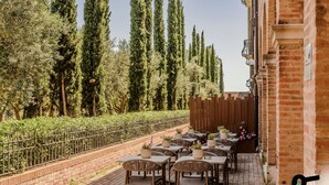 An outdoor patio with tables and chairs, surrounded by a brick wall and tall trees. - Hotiday Venezia Cape (Venice)