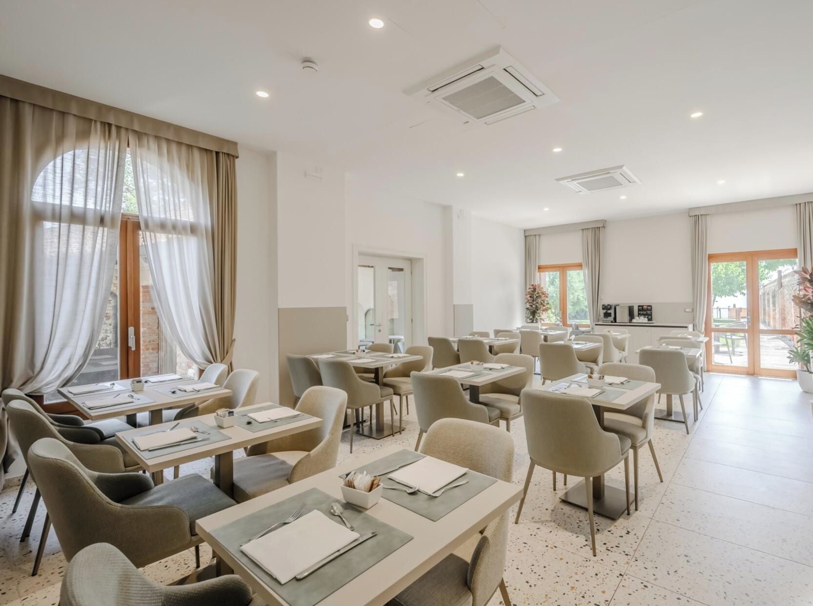 Een restaurantgedeelte in een hotel, met gedekte tafels voor gasten, een keuken op de achtergrond en uitzicht door de ramen.