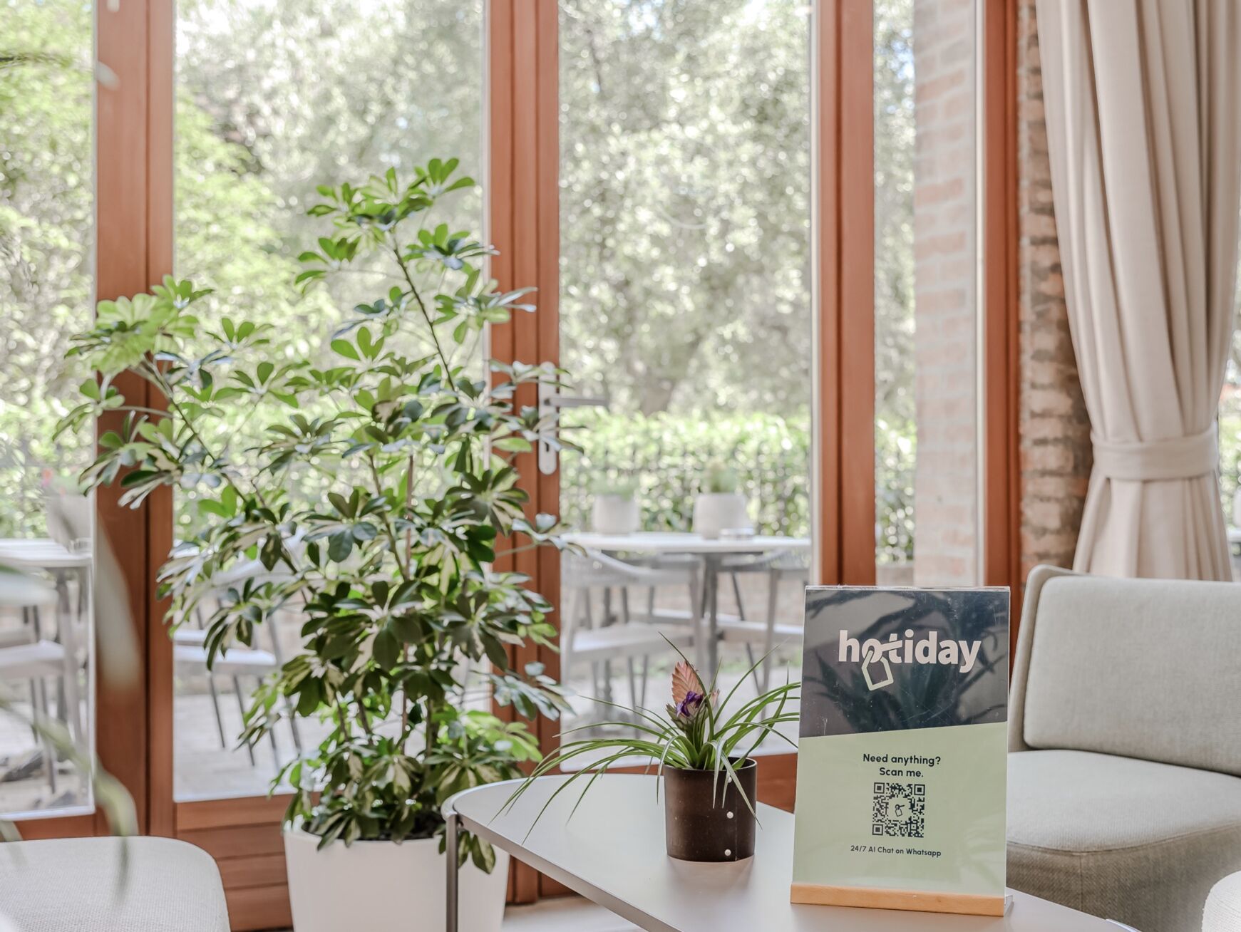 A cozy indoor seating area with a table, a potted plant, and a sign for 'hotday' offering a 24/7 chat service on WhatsApp.