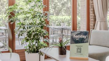 A cozy indoor seating area with a table, a potted plant, and a sign for 'hotday' offering a 24/7 chat service on WhatsApp.