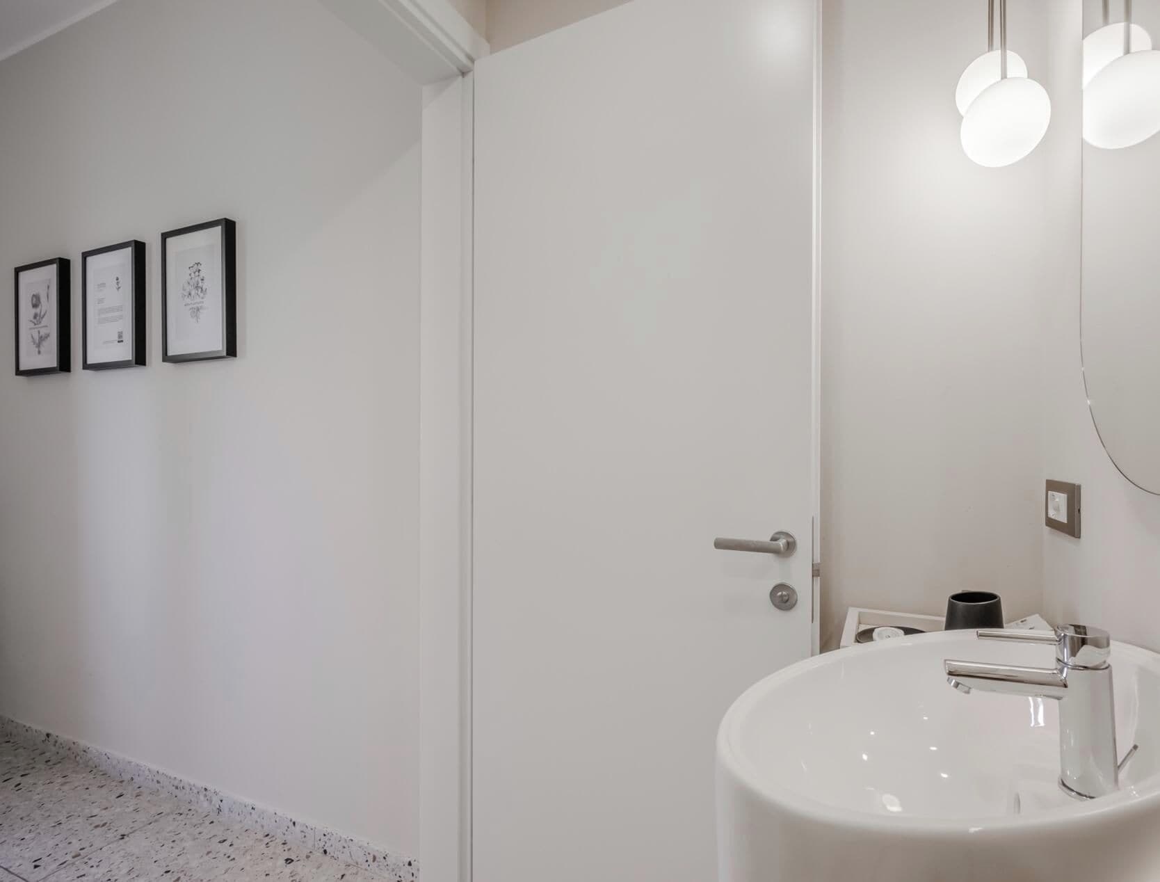 Un baño moderno con un lavabo blanco, una puerta y tres cuadros en la pared.
