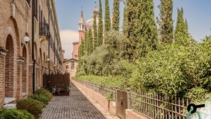 A narrow brick pathway flanked by tall trees and a building with arched windows and a tower. - Hotiday Venezia Cape (Venice)
