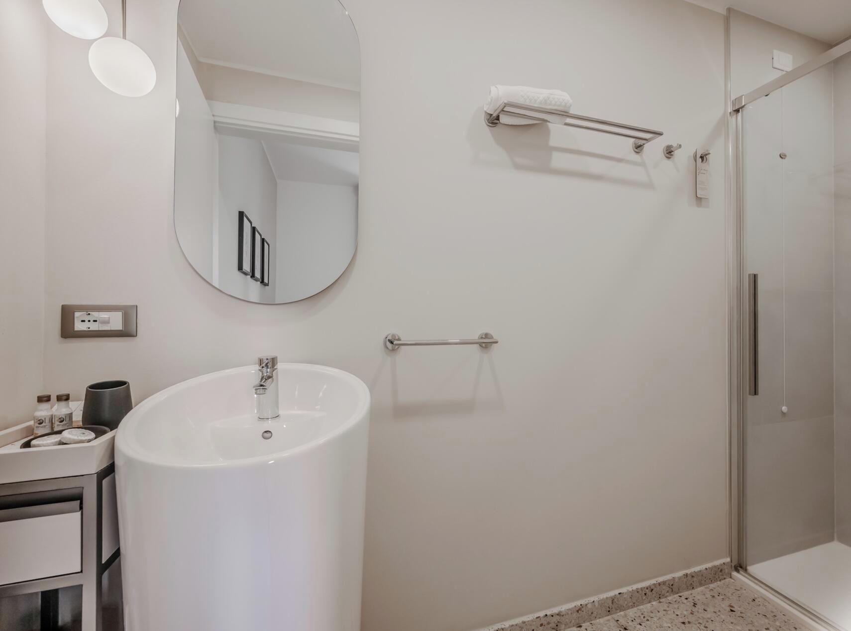 A modern bathroom with a white sink, a mirror, a towel rack, and a glass shower enclosure.