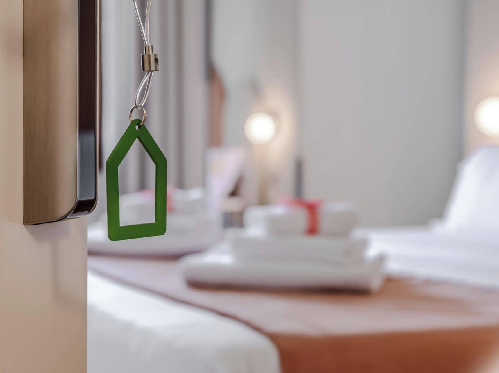 Een hotelkamer met een net opgemaakt bed, een groene sleutelhanger en een zichtbare deurklink.