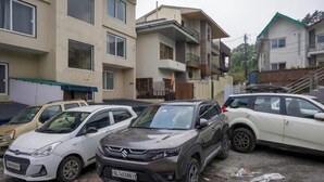 En parkeringsplats med flera bilar, bland annat en vit sedan, en grå SUV och en vit kombi.