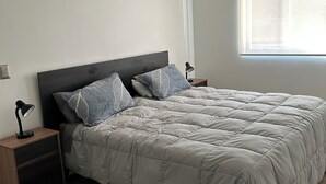 A bedroom with a bed, nightstands, a lamp, and a window. - Departamento acojedor en Parque mar4 Piso 1 (El Tabo)