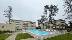 A swimming pool surrounded by a white fence, with a building complex in the background. - Departamento acojedor en Parque mar4 Piso 1 (El Tabo)