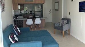 A modern living room with a blue sectional sofa, a grey armchair, and a small dining area with two white chairs. - Departamento acojedor en Parque mar4 Piso 1 (El Tabo)