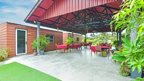 Une terrasse extérieure avec des tables et des chaises, un espace abrité avec un toit rouge et des plantes en pot.