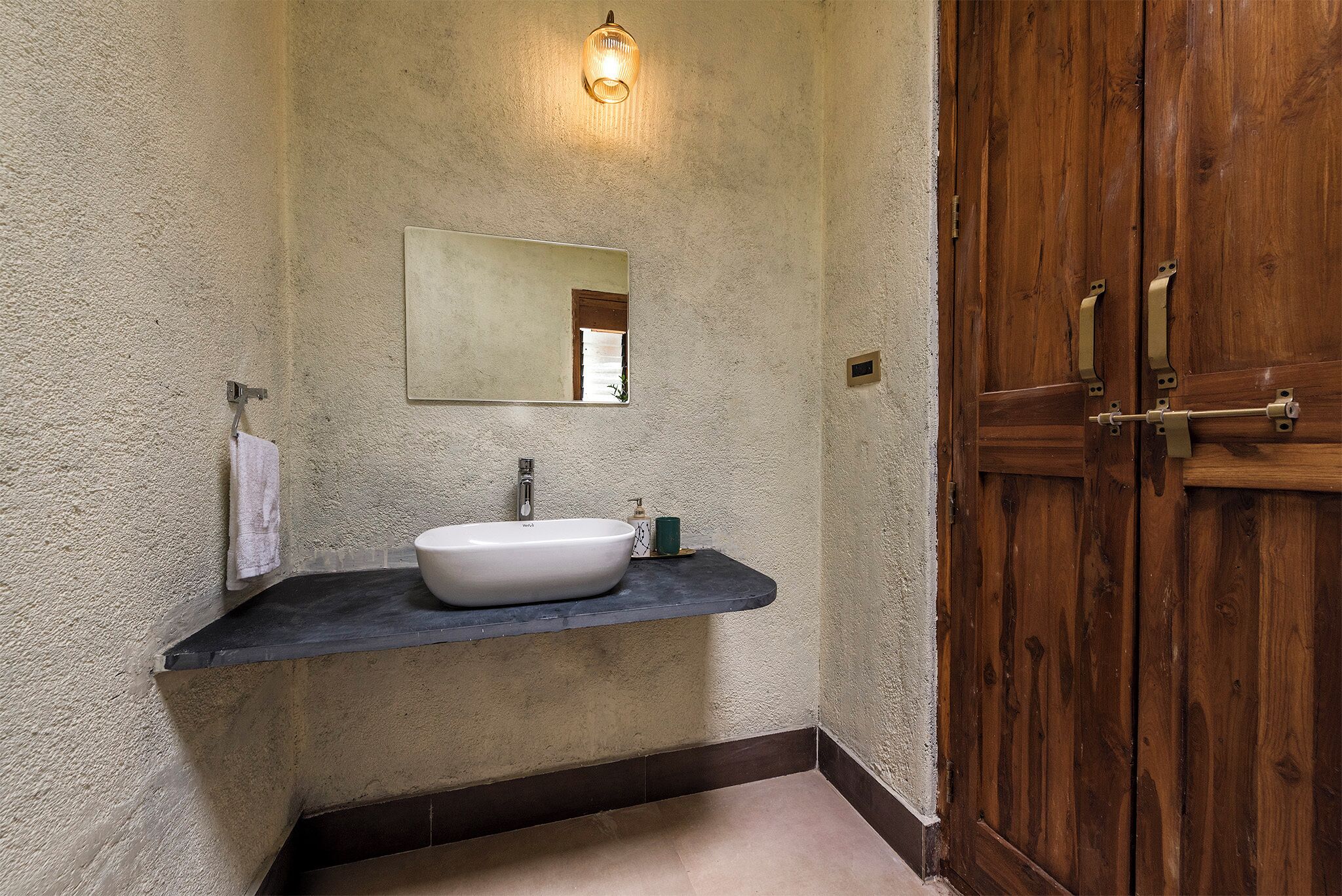Une salle de bain avec un lavabo blanc, un miroir et une porte en bois.