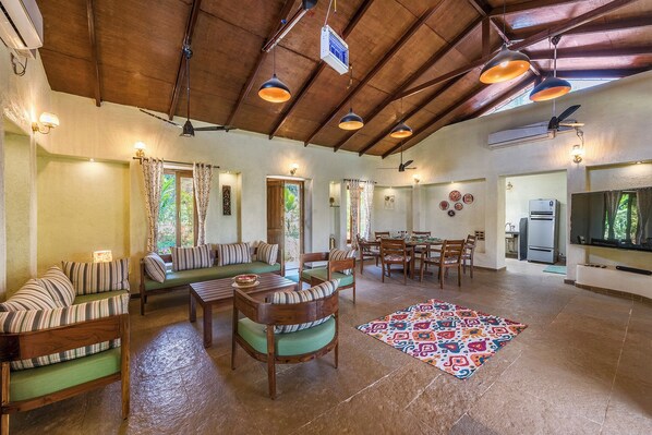 A spacious living area with a high ceiling, wooden furniture, and a colorful rug.