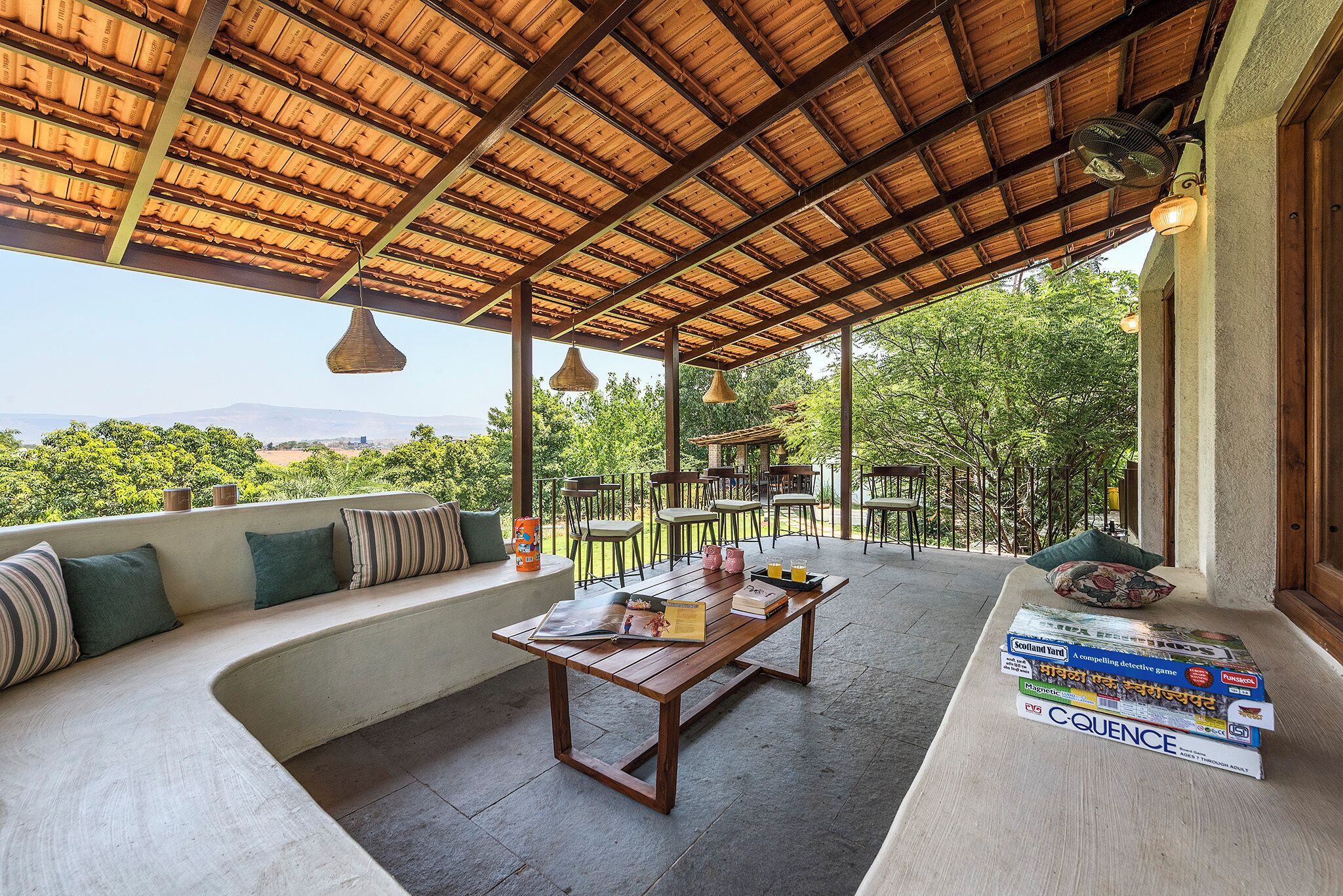 Un área de estar al aire libre techada con una mesa de madera y libros, con vistas a un paisaje pintoresco.
