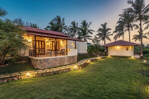 A two-story house with a stone foundation and a red-tiled roof, surrounded by a well-maintained lawn and palm trees.